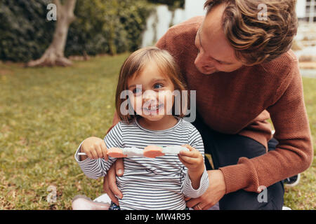 Smiling girl sitting avec son père à l'extérieur tenant un bâton de sucre candy. Père et fille de passer du temps ensemble manger du sucre candy. Banque D'Images