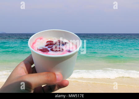 Une tasse de haricots rouge sucrée au red ice dans la main sur la plage. Banque D'Images