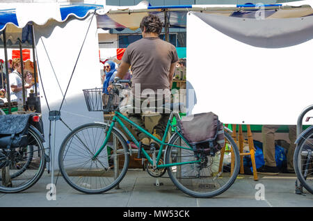 Un homme est assis sur un support à bicyclettes derrière une échoppe de marché sur la rue King à Hammersmith, Londres. Banque D'Images