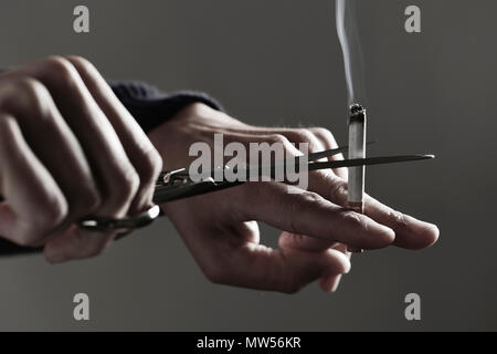 Libre d'un jeune homme de race blanche avec une cigarette allumée à la coupe ciseaux, illustrant le concept de cesser de fumer Banque D'Images