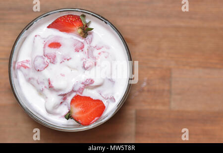 L'importance de la glace à la vanille avec des tranches de fraises dans un bol en verre. Debout sur une table en bois Banque D'Images