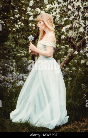 Femme debout dans la région de apple blossom holding bunch of bluebell flowers Banque D'Images