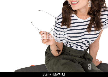 Cropped shot of smiling girl sitting on skateboard et holding eyeglasses Banque D'Images