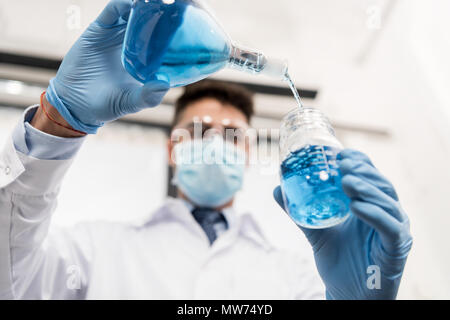 Jeune professionnel scientifique au masque stérile, versant dans le réactif de laboratoire jar Banque D'Images