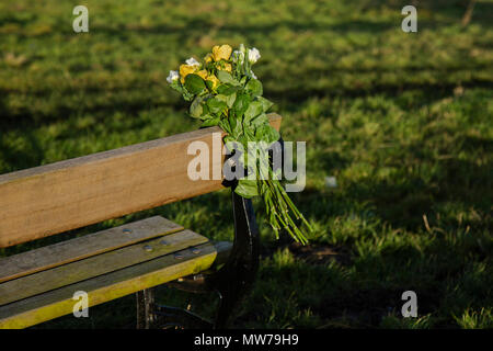 Un bouquet de fleurs ont été attachés à un banc en bois dans la mémoire d'un être cher. Banque D'Images