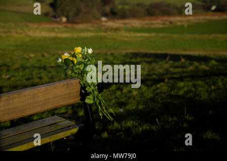 Un bouquet de fleurs ont été attachés à un banc en bois dans la mémoire d'un être cher. Banque D'Images