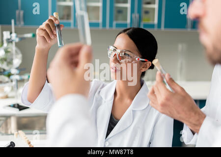 Les jeunes scientifiques en blouse blanche l'examen de tubes à essai avec les réactifs en laboratoire chimique Banque D'Images