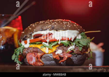 Fresh burger classique avec du boeuf, fromage, bacon, oignons, tomates et roquette sur table en bois. Banque D'Images