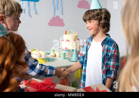 Les garçons se serrer la main alors que les filles holding gifts at Birthday party Banque D'Images