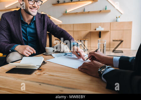 Smiling businessman pointing at contrat que collègue gestuelle au cours de réunion de cafe Banque D'Images