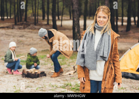 Happy woman looking at camera, tandis que son mari et kids camp sur la nature Banque D'Images