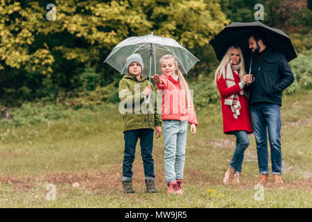 Adorables petits enfants et jeunes parents des parasols in autumn park Banque D'Images