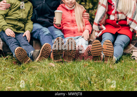 Cropped shot de famille portant des chaussures d'automne et assis ensemble dans park Banque D'Images