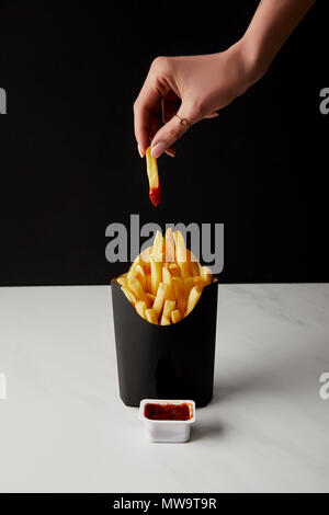 Cropped shot of woman folding french fry versé dans le ketchup plus fort de frites isolated on black Banque D'Images