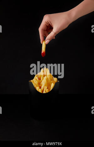 Cropped shot of woman folding french fry versé dans le ketchup plus fort de frites isolated on black Banque D'Images