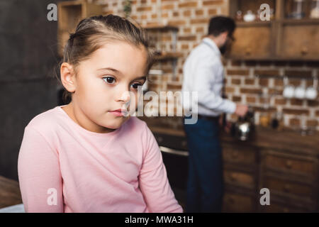 Ennuyer petit enfant à la voiture tandis que le petit-déjeuner de cuisson père en arrière-plan flou Banque D'Images