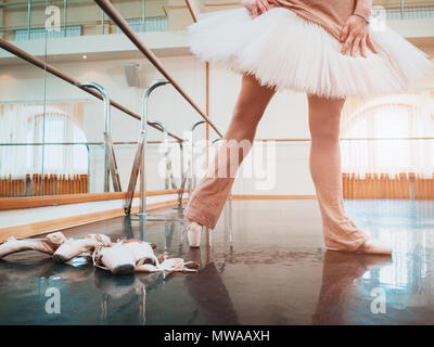 Ballerine en tutu blanc et pointe de ballet s'étend sur barre en salle de sport. Femme pratiquant au studio de danse. Travail de jeune fille. Banque D'Images