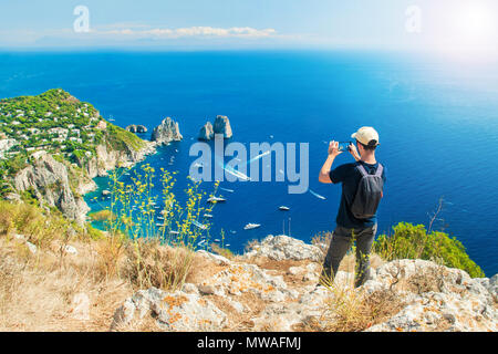 Young caucasian tourist taking picture de célèbres Faraglioni en mer avec son smartphone sur le sommet du Mont Solaro après une randonnée le sentier sur Capri Banque D'Images