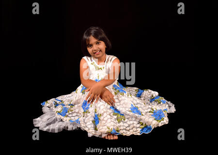 Petite fille avec un sourire mignon à la caméra à l'encontre d'une toile de fond noir Banque D'Images