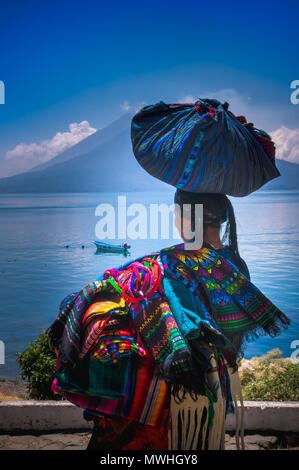 Panajachel, Guatemala - Avril, 25, 2018 : vue extérieure de la femme indigène non identifiée, portant des vêtements typiques et la marche à lakeshore avec petits bateaux dans le lac Atitlan et le volcan en arrière-plan au Guatemala Banque D'Images