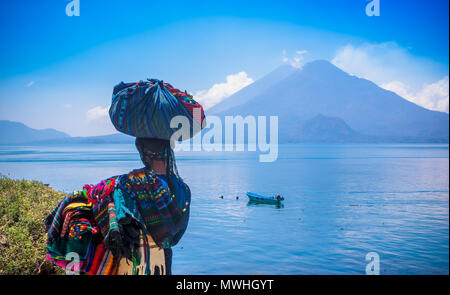 Panajachel, Guatemala - Avril, 25, 2018 : vue extérieure de la femme indigène non identifiée, portant des vêtements typiques et la marche à lakeshore avec petits bateaux dans le lac Atitlan et le volcan en arrière-plan au Guatemala Banque D'Images