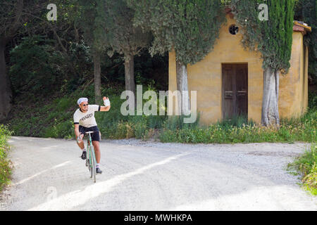 Cycliste passant à vélo devant une petite église et des cyprès à Lucignano d'Asso, prenant part à l'Eroica Montalcino, Sienne, Toscane, Italie en mai Banque D'Images