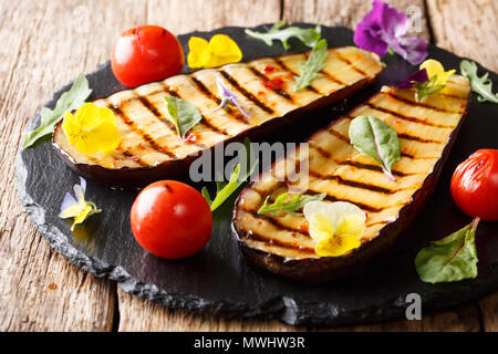 Sain et Délicieux grillés aubergines tomates aux fines herbes et fleurs comestibles close-up sur la table horizontale. Banque D'Images