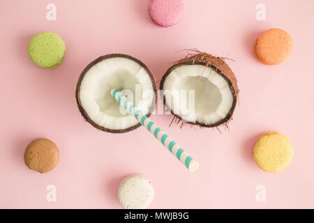 Les moitiés de noix de coco avec paille et macarons sur fond rose pastel un minimum de concept créatif. Banque D'Images