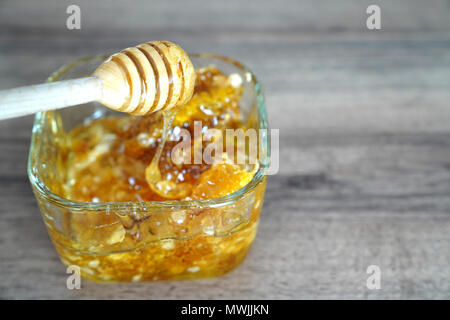 Balancier en bois quadrangulaire avec bol en verre de miel sur la table de noyer foncé Banque D'Images