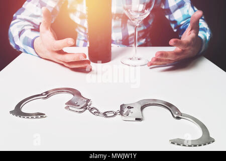 La dépendance à l'alcool, vous libérer de l'alcool, des problèmes avec la vodka, le vin. Il y a des menottes sur la table, dans l'arrière-plan un homme avec des bras sp Banque D'Images