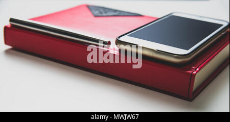 Il y a un calendrier, un téléphone et un stylo sur la table. Contact concept, formulaire de contact. Calendrier rouge, blanc téléphone avec écran vide, argent Banque D'Images