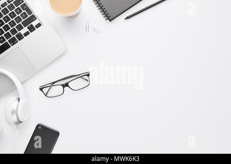 L'espace de travail concept. Vue de dessus de l'ordinateur portable, un casque blanc, noir téléphone cellulaire, ordinateur portable, lunettes et café sur fond blanc avec l'exemplaire de l'espace. Mise à plat Banque D'Images