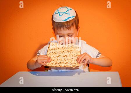 Happy little enfant juif avec une kippa sur la tête de manger du pain azyme pendant la fête juive de Pessah. Illustration de la Pâque. Banque D'Images