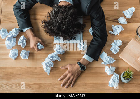 Vue supérieure de l'homme fatigué couché sur table avec des papiers froissés Banque D'Images