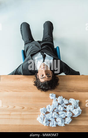 Vue supérieure de l'homme fatigué couché sur table avec des papiers froissés Banque D'Images