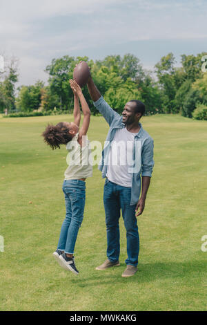 African American petite fille et père s'amusant avec ballon de rugby in park Banque D'Images