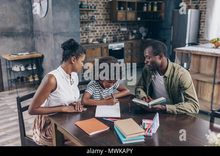 Petite fille écrit à son portable à la table de la cuisine avec ses parents, assis près d'elle Banque D'Images