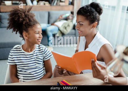 Maman tenant un ordinateur portable et fille assis ensemble au bureau, smiling at each other Banque D'Images