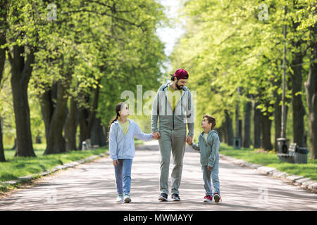 Smiling père tenant la main de son fils et sa fille et walking in park Banque D'Images