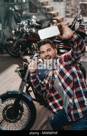 Happy handsome man with rock signer en tenant sur smartphone selfies avec moto classique Banque D'Images