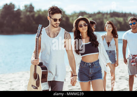 Heureux l'interracial couple holding hands et passer du temps avec leurs amis on beach Banque D'Images