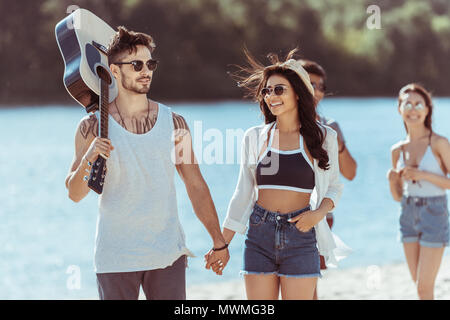 Heureux l'interracial couple holding hands tandis que l'homme l'exécution de la guitare sur Riverside Banque D'Images