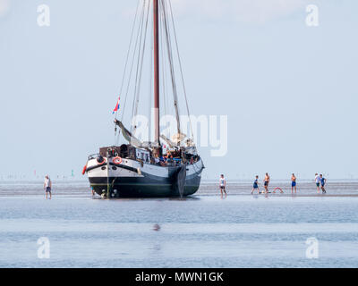 Groupe de jeunes jouant sur sable et séché à fond plat de yacht à voile à marée basse sur la mer des Wadden, Pays-Bas Banque D'Images