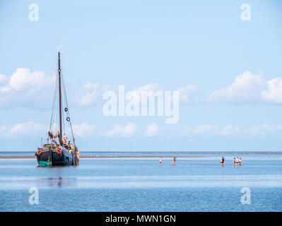 Groupe de jeunes de patauger dans l'eau peu profonde et yacht à échoué à marée basse sur la mer des Wadden, Pays-Bas Banque D'Images