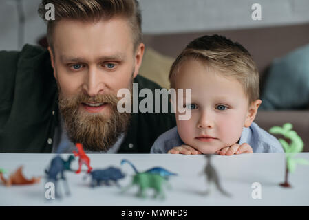 Focus sélectif de père et petit fils à la recherche de dinosaures jouets disposés sur la table d'ensemble à la maison Banque D'Images