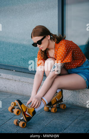 Fille élégante en patins à porter des lunettes alors qu'il était assis sur la rue Banque D'Images