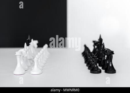 Les chiffres d'échecs en rangées sur la table blanche près de mur noir et blanc Banque D'Images