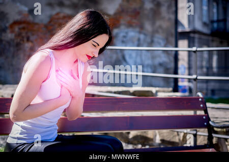 Woman is holding sa poitrine. crise cardiaque. Park et à l'extérieur. Par rapport au travail, fatigué, malade. Banque D'Images