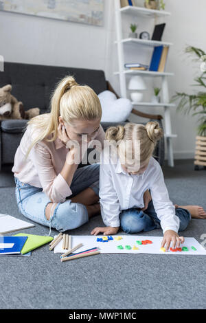 Mère fille avec peu de chiffres d'apprentissage tout en étant assis sur le plancher à la maison Banque D'Images