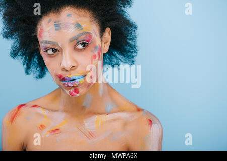 Jolie jeune femme avec des traits de peinture sur le visage à l'écart isolé sur blue Banque D'Images